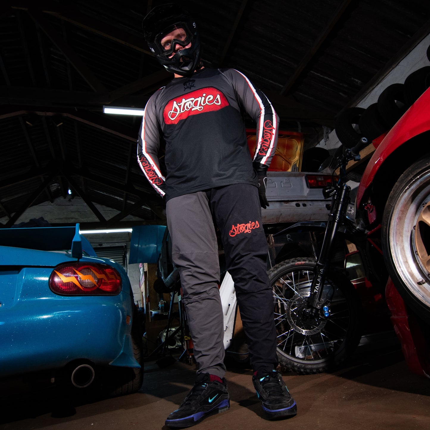 Person wearing a helmet and racing suit standing next to a red car in a garage.